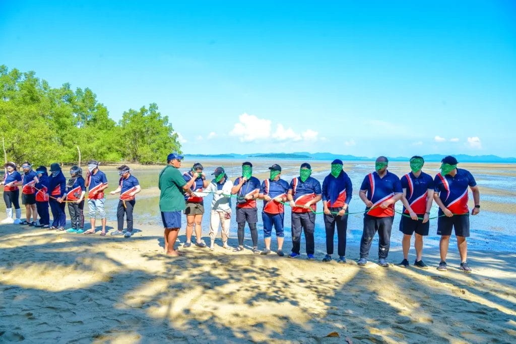 Blindfold teams playing a game holding a rope in their hands with beautiful tropical beach and sea background